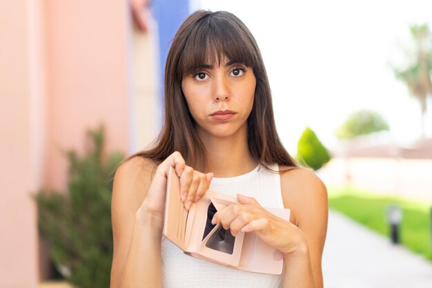 Mujer joven al aire libre sosteniendo una billetera y con expresión triste