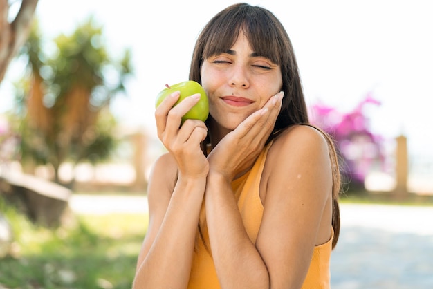 Mujer joven al aire libre sosteniendo una manzana con expresión feliz