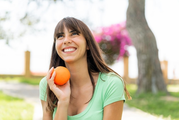 Mujer joven al aire libre sosteniendo una naranja con expresión feliz