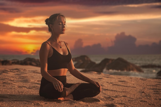 Mujer joven al atardecer hace yoga para un estilo de vida saludable en el mar tropical o en la playa del océano al aire libre