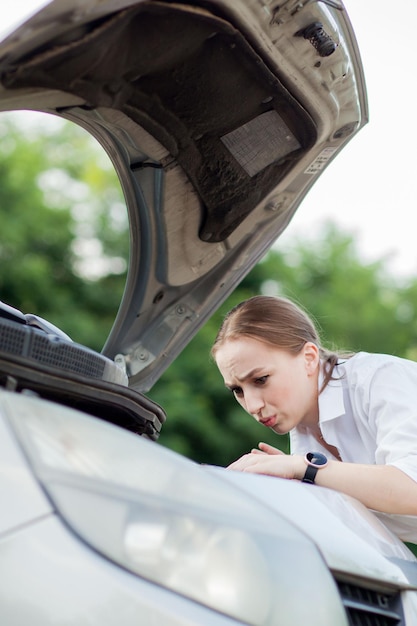 Mujer joven al costado del camino después de que su auto se descompuso Ella abrió el capó para ver el daño