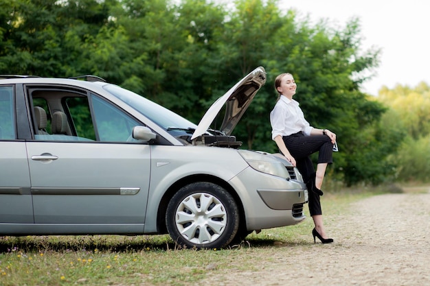 Mujer joven al costado del camino después de que su auto se descompuso Ella abrió el capó para ver el daño