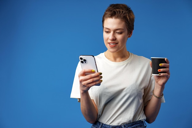 Foto mujer joven alegre y atractiva que sostiene un teléfono inteligente que disfruta chateando o comprando en línea contra azul