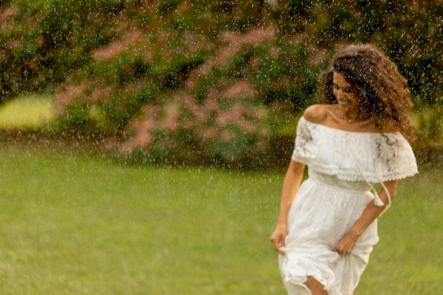 Mujer joven alegre atrapada por la lluvia de verano en el parque