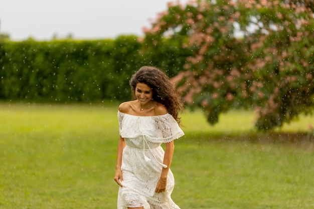 Mujer joven alegre atrapada por la lluvia de verano en el parque