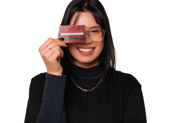Mujer joven alegre con cabello negro cubre un ojo con una tarjeta de crédito roja