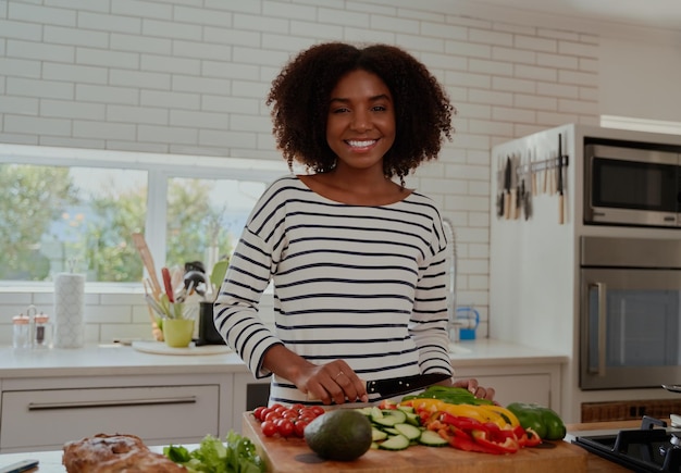 Mujer joven alegre con cabello rizado cortando verduras para ensalada en una cocina moderna