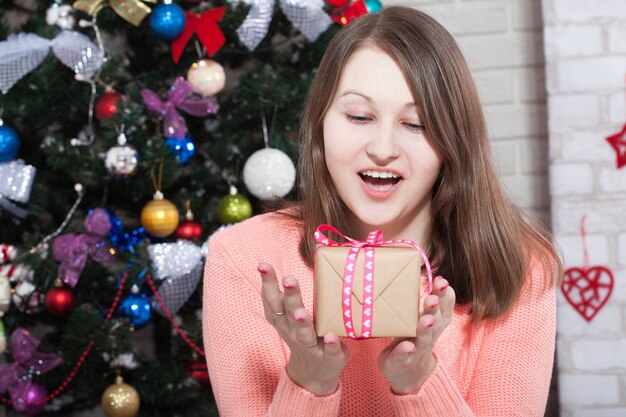 Mujer joven alegre con caja de regalo en manos disfrutando de la Navidad en casa