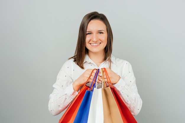 Mujer joven alegre en la celebración informal de coloridos bolsos de compras sobre fondo gris