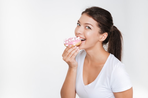 Mujer joven alegre comiendo sabroso buñuelo aislado sobre pared blanca