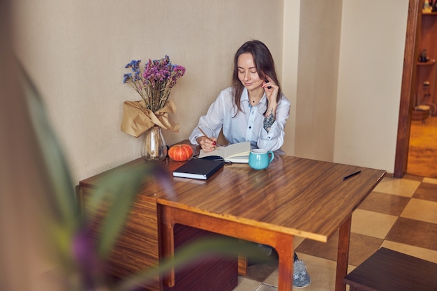 Foto mujer joven alegre confiada y feliz está disfrutando del té mientras lee el libro en su cocina en casa