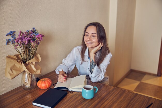 Mujer joven alegre confiada y feliz está disfrutando del té mientras lee el libro en su cocina en casa