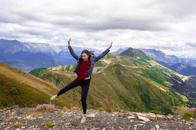 Mujer joven alegre después de una exitosa caminata divertida salta en la cima de la montaña
