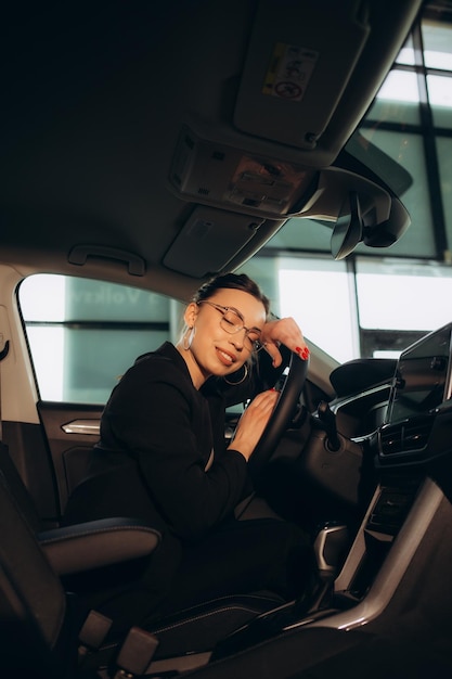 Mujer joven y alegre disfrutando de un coche nuevo abrazando el volante sentada en el interior Mujer conduciendo un coche nuevo Mujer conductor retrato en el coche