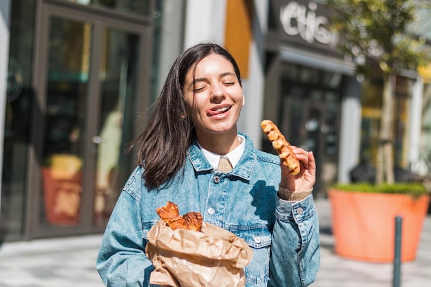 Mujer joven alegre disfrutando de sabrosos gofres frente a un café en la calle. llevar comida en la ciudad