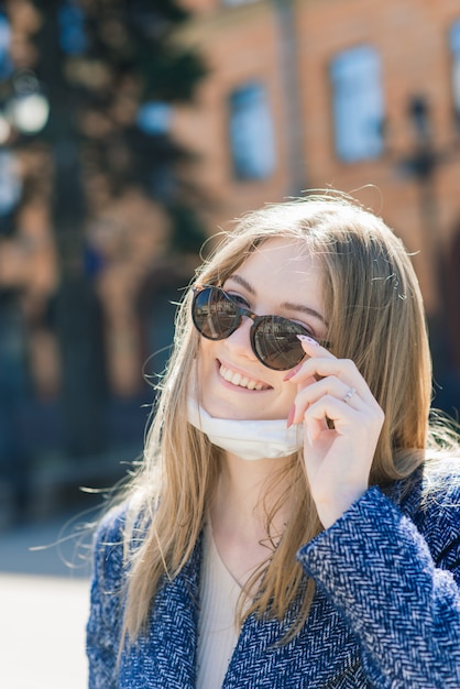 Mujer joven alegre feliz quitando la mascarilla médica mientras está de pie en la calle en la ciudad.