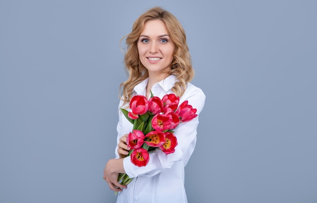 Mujer joven alegre con flores de tulipán de primavera sobre fondo gris