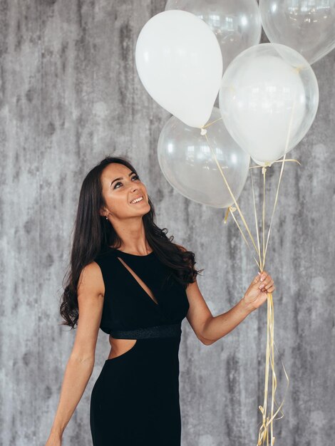 Foto mujer joven alegre con globos de pie y sonriendo