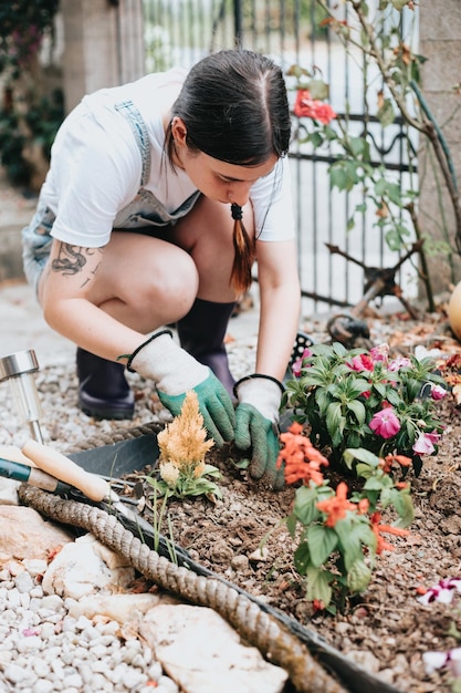 Mujer joven alegre en guantes usando herramientas de jardinería para plantar flores en el patio trasero informal