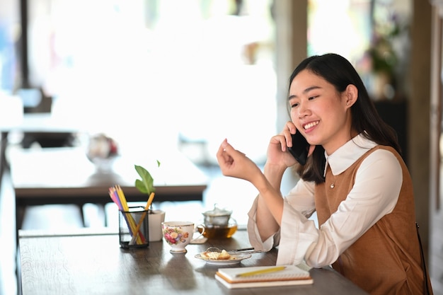 Mujer joven alegre hablando por teléfono móvil mientras se ubica en la cafetería moderna