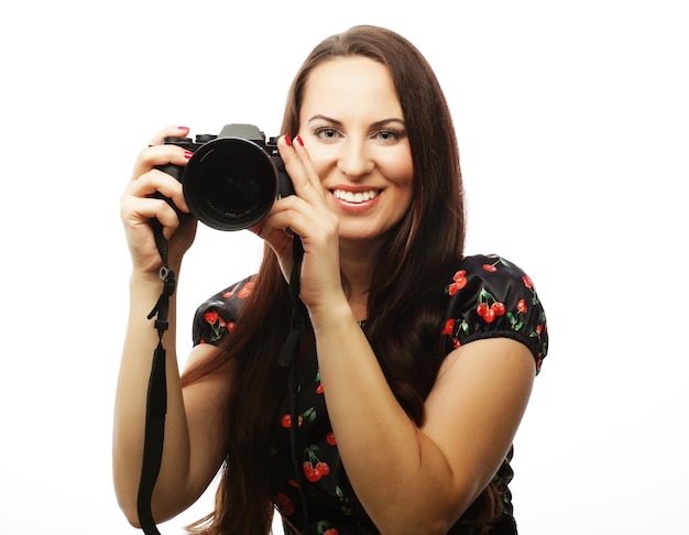 Mujer joven alegre haciendo fotos en la cámara sobre fondo blanco.