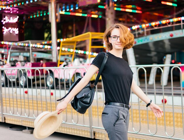 Mujer joven alegre hipster en gafas y sombrero en el parque de atracciones