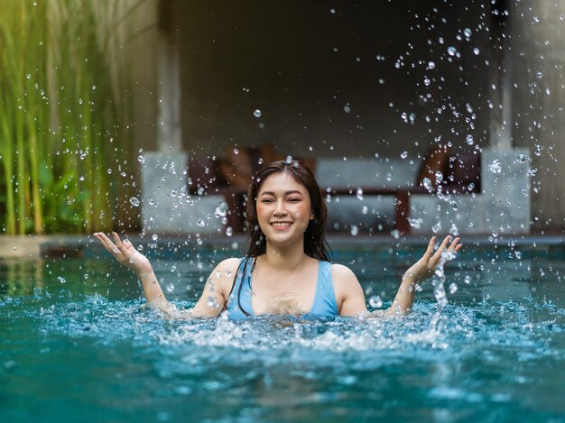 Mujer joven alegre jugando agua chapoteando en la piscina