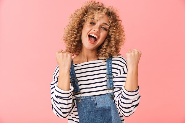 Mujer joven alegre con pelo rizado vistiendo ropa casual, celebrando el éxito