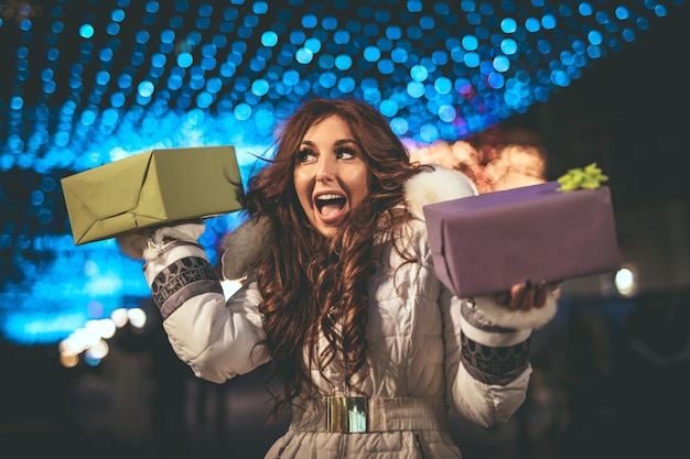 Mujer joven alegre con presente divirtiéndose en la calle de la ciudad en Navidad.