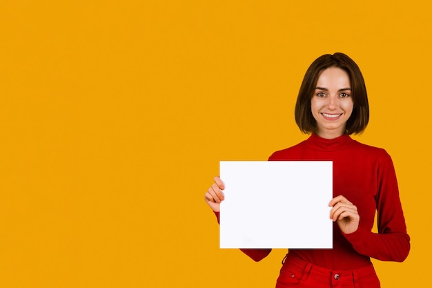 Mujer joven alegre que muestra el tablero publicitario en blanco blanco