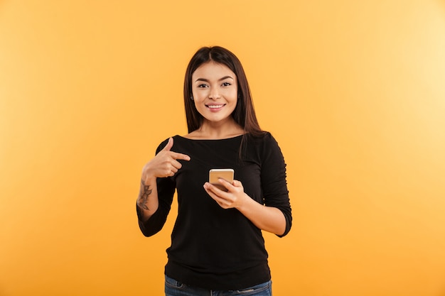 Mujer joven alegre que señala usando el teléfono móvil.