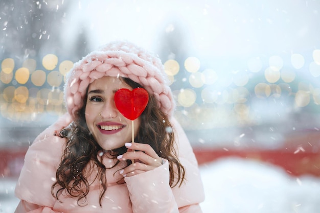 Mujer joven alegre que sostiene la piruleta roja en forma de corazón. Espacio para texto