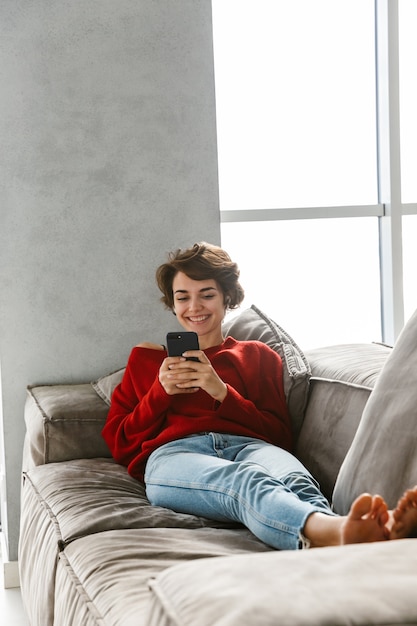 Mujer joven alegre relajándose en casa, escuchando música con auriculares inalámbricos