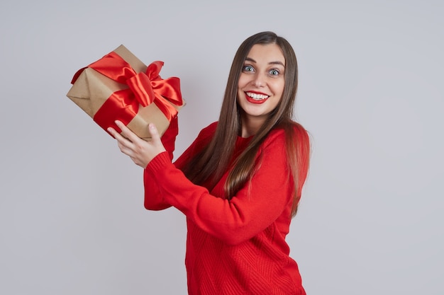 Mujer joven alegre en un suéter rojo sosteniendo una caja de regalo