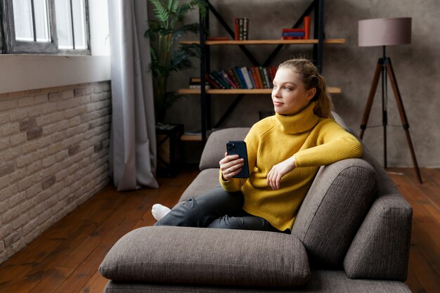 Mujer joven alegre mediante teléfono móvil mientras está sentado en un sofá en casa.