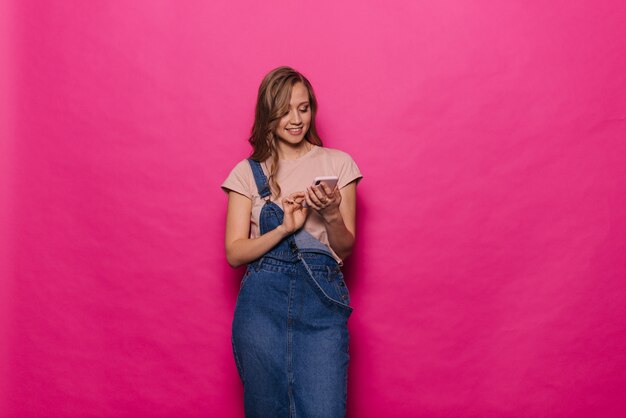 Mujer joven alegre con teléfono móvil sobre fondo rosa aislado