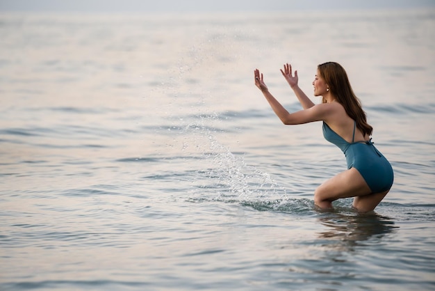 Mujer joven alegre en traje de baño jugando agua salpicando en la playa del mar en la isla de Koh Chang Tailandia