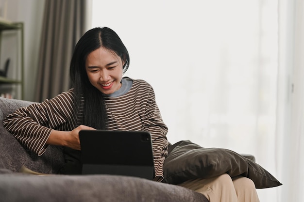 Mujer joven alegre usando tableta digital en el sofá en casa jugando o comprando en línea