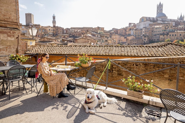 Mujer joven almorzando sentada con un perro en un restaurante al aire libre en la ciudad de siena