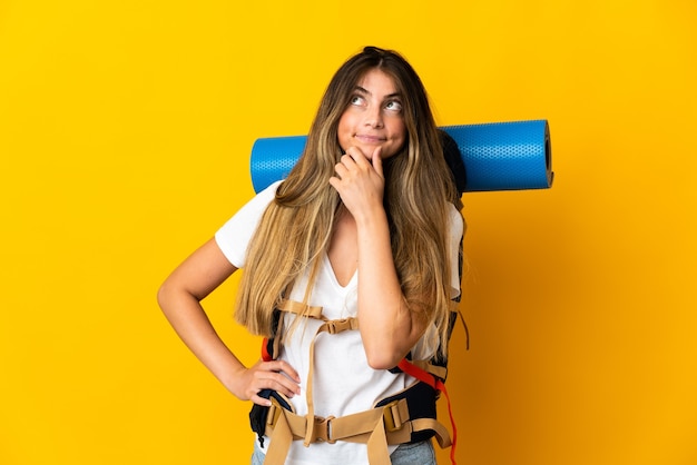 Mujer joven alpinista con una gran mochila aislada en amarillo con dudas