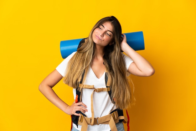 Mujer joven alpinista con una gran mochila aislada en amarillo con dudas