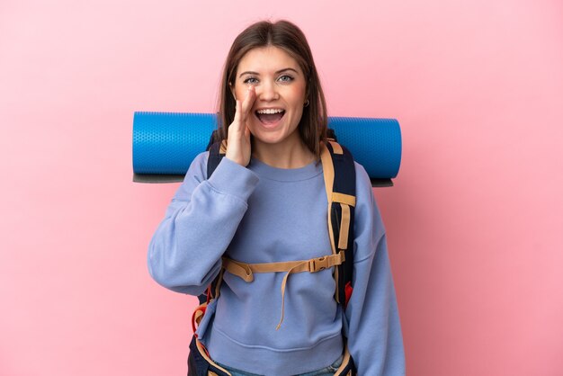 Mujer joven alpinista con una gran mochila aislada en la pared rosa gritando con la boca abierta