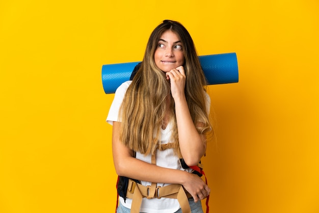 Mujer joven alpinista con una gran mochila en amarillo con dudas y pensamiento