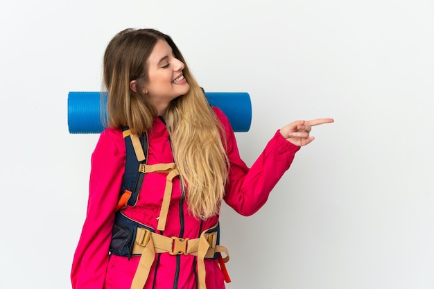 Mujer joven alpinista con una gran mochila sobre espacio aislado apuntando con el dedo hacia un lado y presentando un producto