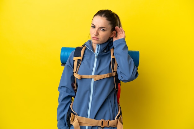 Mujer joven alpinista con una gran mochila sobre fondo amarillo aislado que tiene dudas