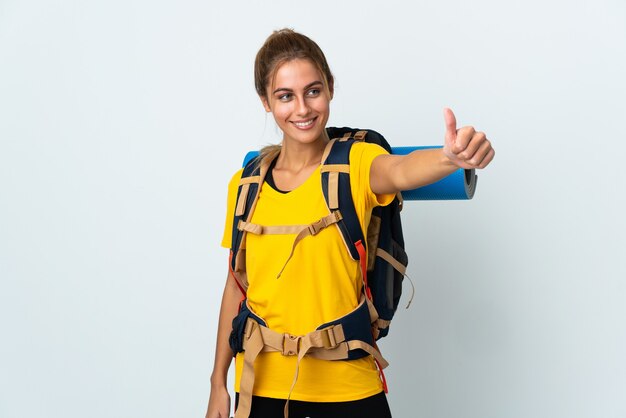 Mujer joven alpinista con una mochila grande aislado sobre fondo blanco dando un pulgar hacia arriba gesto