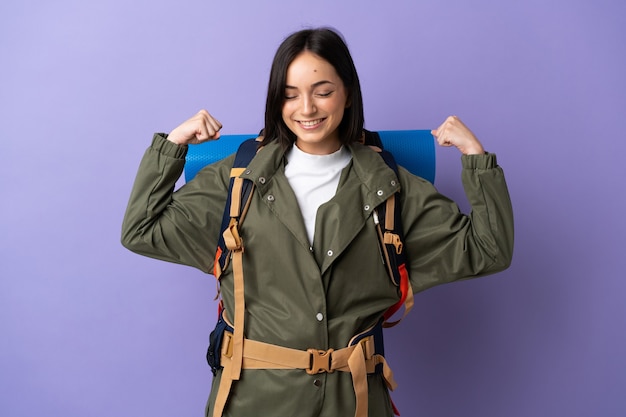 Mujer joven alpinista con una mochila grande sobre fondo aislado haciendo un gesto fuerte