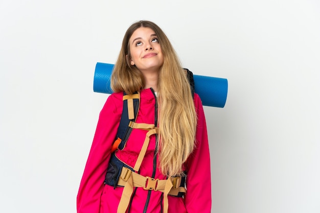 Mujer joven alpinista con una mochila grande sobre fondo aislado y mirando hacia arriba