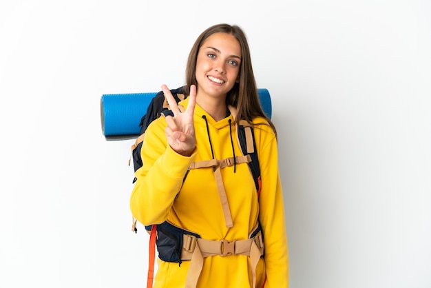 Mujer joven alpinista con una mochila grande sobre fondo blanco aislado sonriendo y mostrando el signo de la victoria