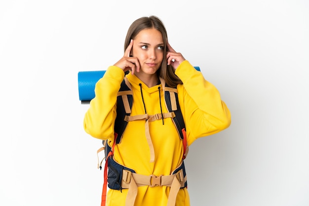 Mujer joven alpinista con una mochila grande sobre fondo blanco aislado teniendo dudas y pensando